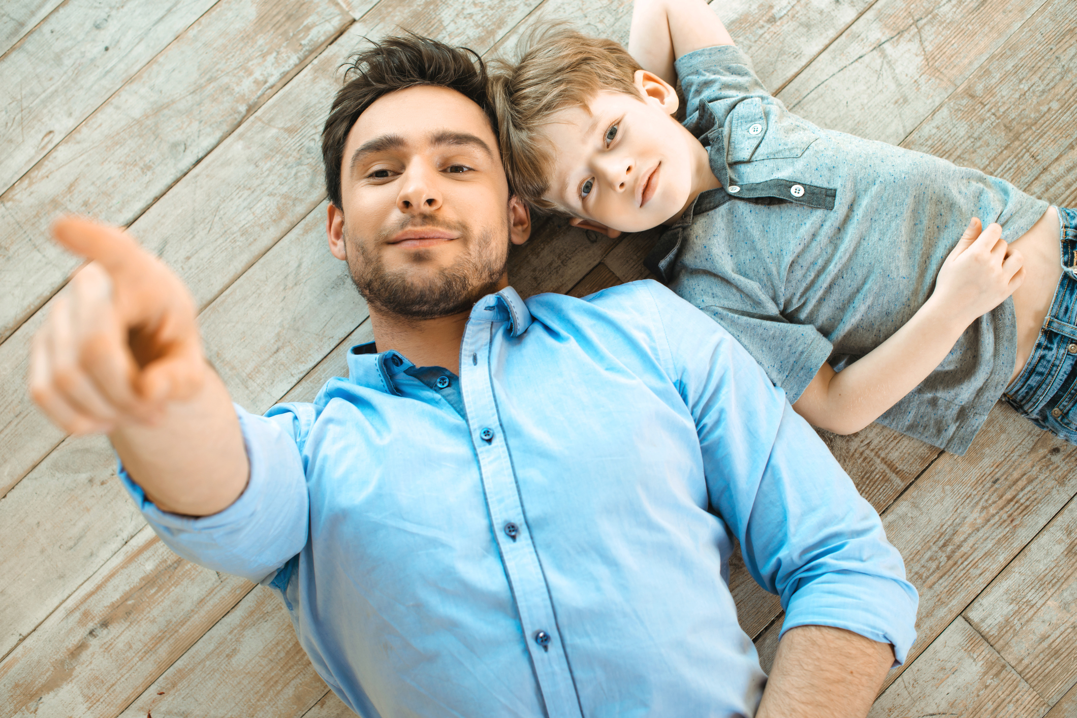 Boy and dad smiling and lying on wooden floor. 